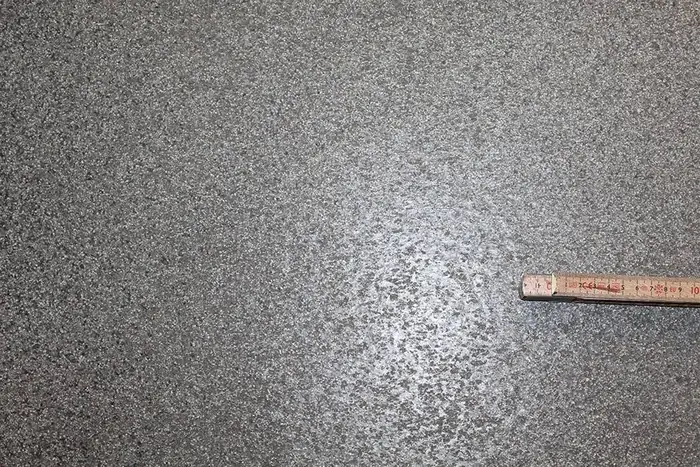 Närbild på ett halkskyddat slitskikt med tumstock som storleksreferens